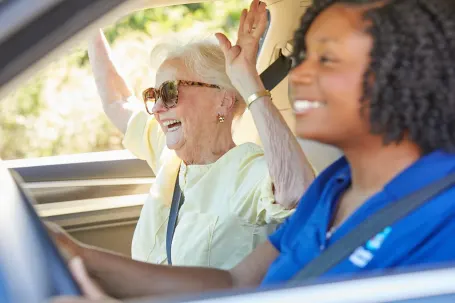 A Comfort Keepers caregiver and a senior client happily driving on a sunny day both smiling warmly.