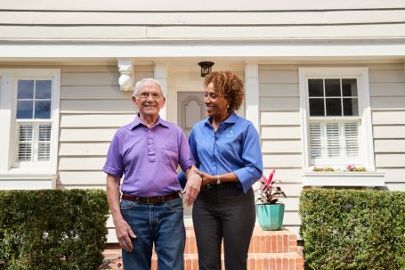 caregiver helping senior man walk down the steps of his home