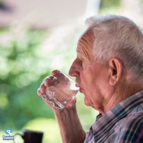 Comfort Keepers client and senior takes a drink from a cold glass of water.