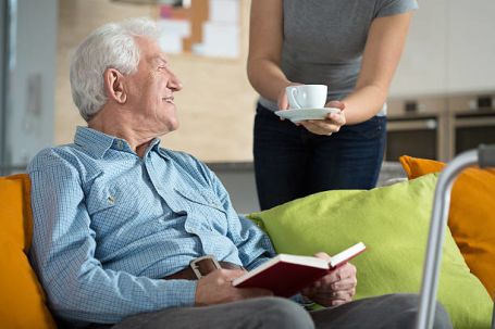 Senior veteran and caregiver having coffee in the living room