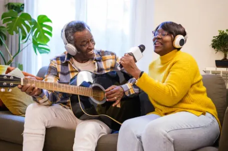 two seniors playing music on the couch, one playing guitar and one singing 
