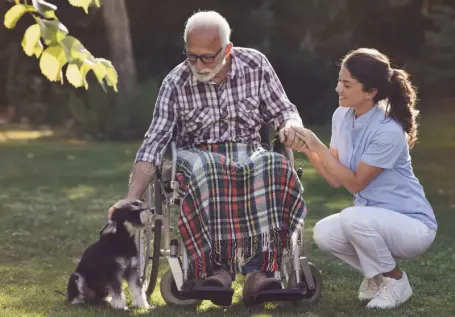 Caregiver and senior in a wheelchair petting dog
