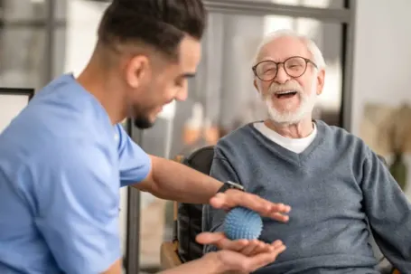 Smiling caregiver and senior man using arthritis flex ball for hand therapy