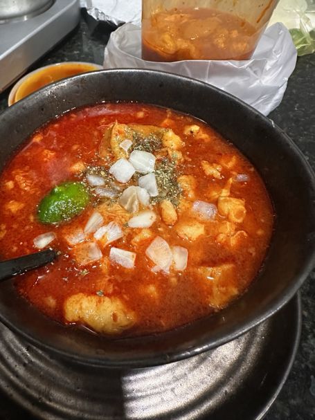 A warm bowl of traditional El Paso menudo with lime and oregano, representing the cultural heritage of senior care. / Delivering takeout food from a favorite El Paso restaurant to a smiling senior client.