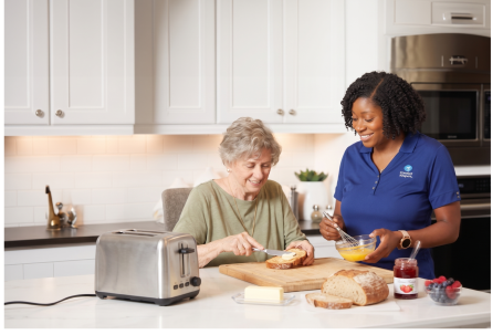 A Comfort Keepers caregiver and an older woman making breakfast together in a sunny Edison kitchen, an example of Interactive Caregiving