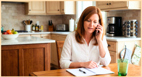 An adult daughter at her kitchen table on the phone taking notes, inquiring about home care for her parent in Edison, NJ