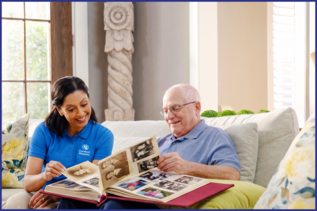 A Comfort Keepers caregiver looking through a photo album with an older man with dementia at home in Cherry Hill, NJ
