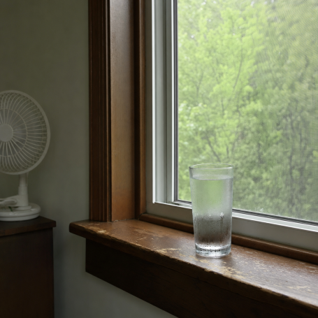 Glass of water on a wooden windowsill with a fan behind, humid Syracuse summer afternoon light