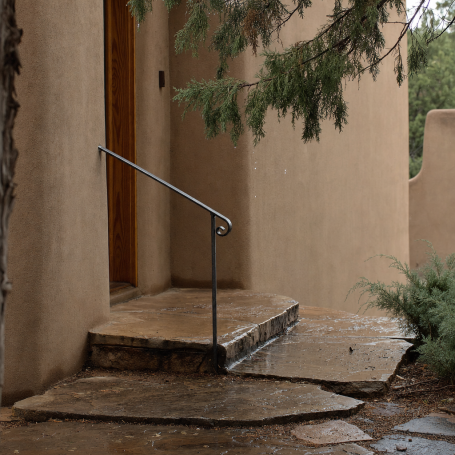 Wet flagstone portal step and iron handrail at a Santa Fe adobe home after a monsoon rain