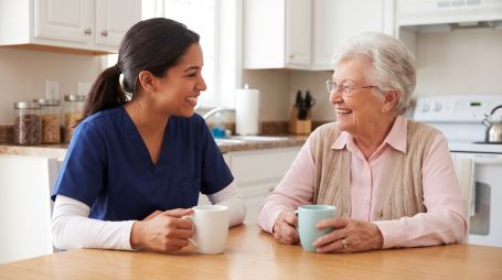 Caregiver and senior sharing lighthearted moment at kitchen table.
