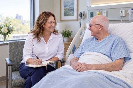 An adult daughter sits with her father in a hospital room, writing in a notebook.