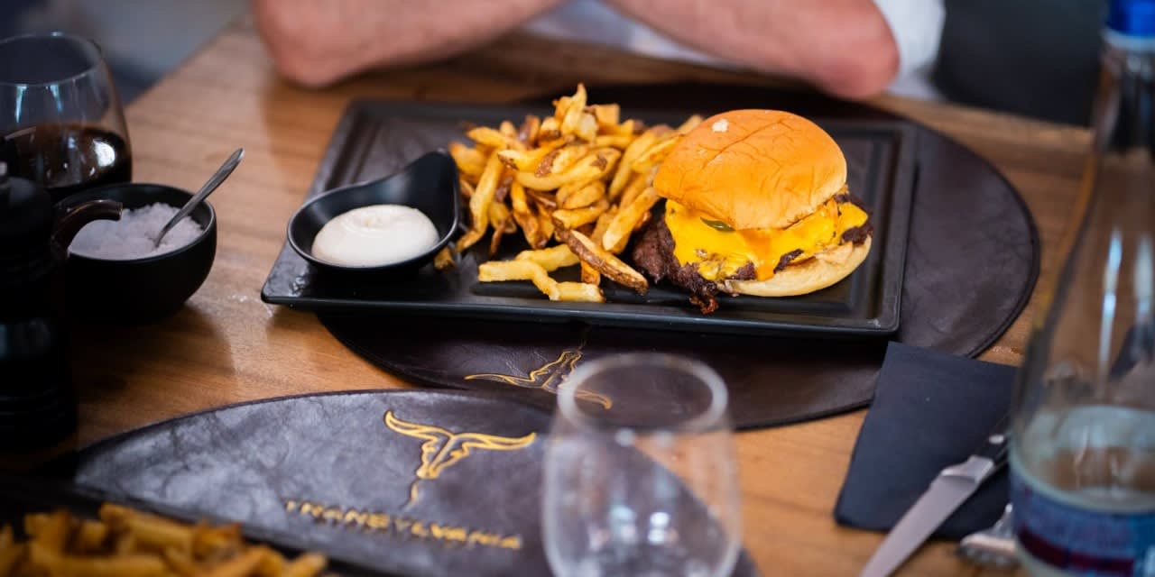 Smashed burger cu cheddar și cartofi prăjiți, servit la masă, pe suportul cu logo Transylvania