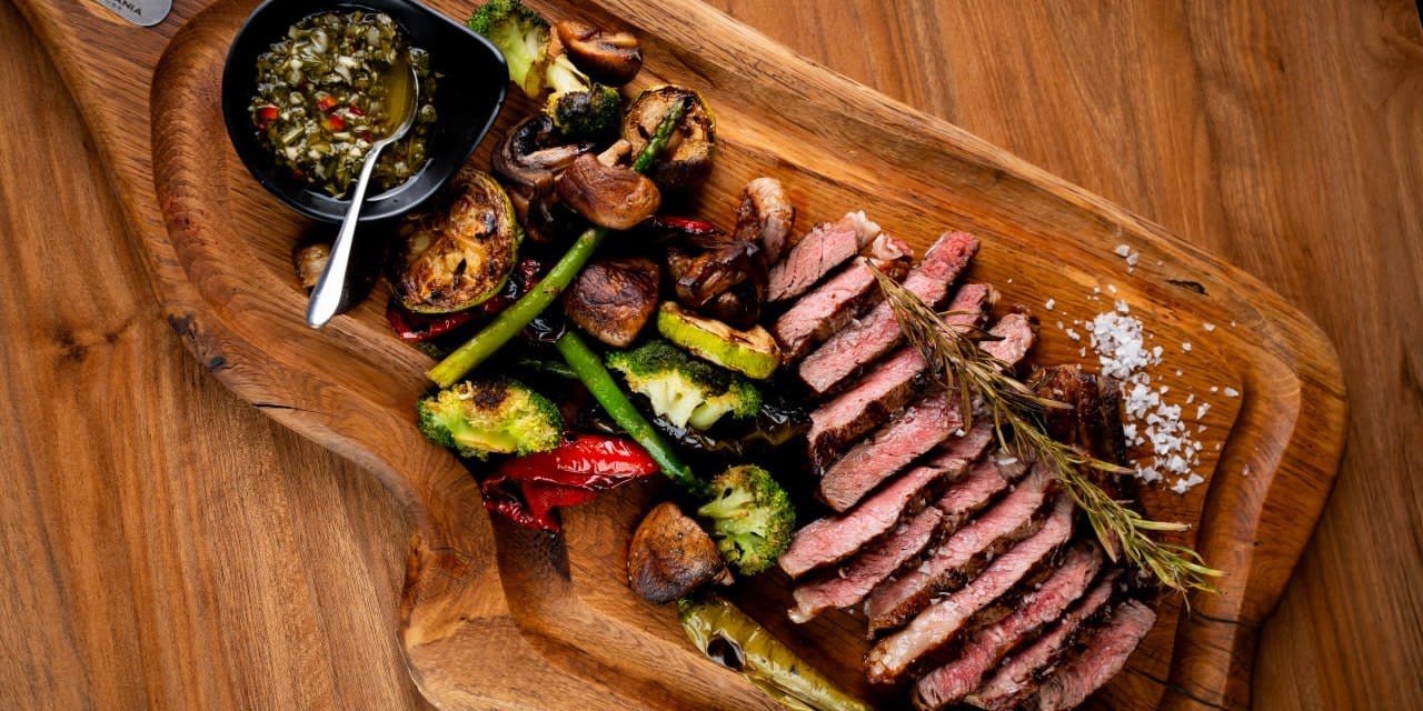Vită feliată pe platou de lemn, cu legume la grătar și chimichurri · Transylvania Steakhouse