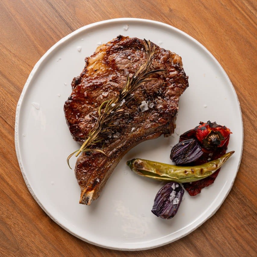 Ribeye cu os pe farfurie albă, cu rozmarin, ardei și ceapă la grătar · Transylvania Steakhouse
