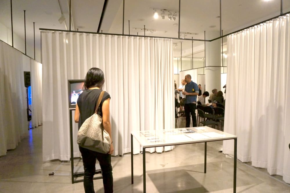 Exhibition installation featuring TV and tabletop surrounded by curtains