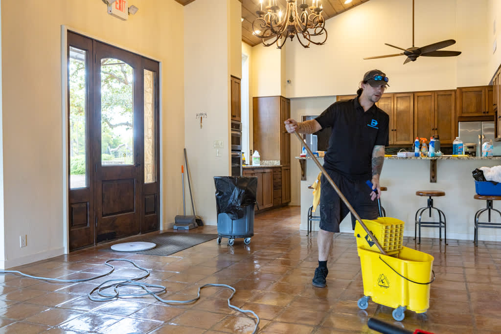 Sanitizing and disinfecting service professional mopping a kitchen floor with a yellow mop bucket.