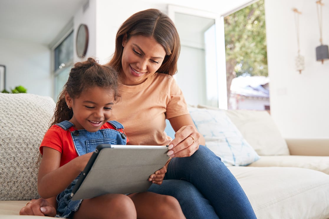 Mother and daughter sitting on couch using tablet together.