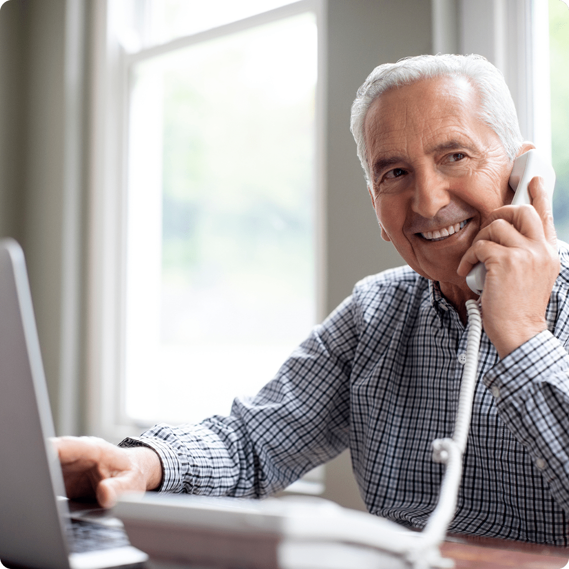 Older man talking on landline phone while using a laptop