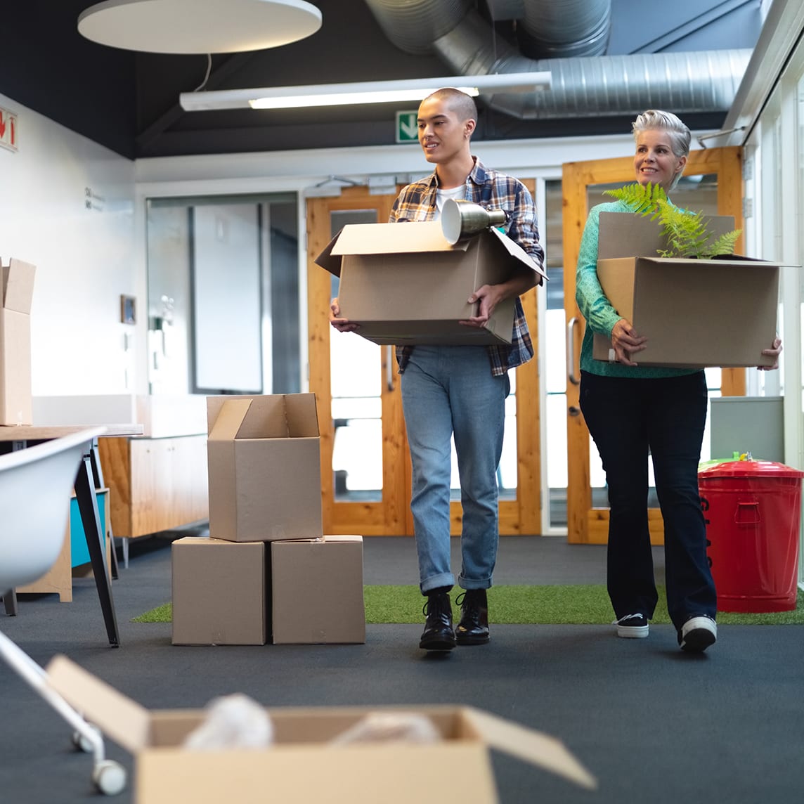 Two co-workers carrying moving boxes through office