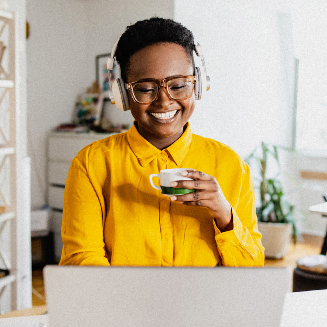 Happy woman wearing yellow drinks tea while on her laptop