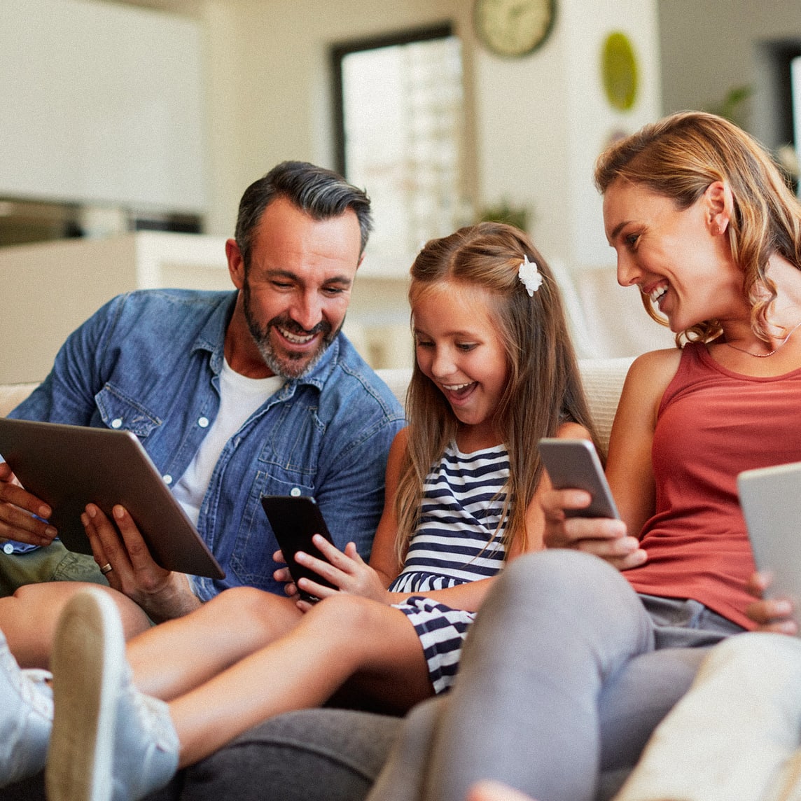 family sitting on couch looking at tablet and smart phones