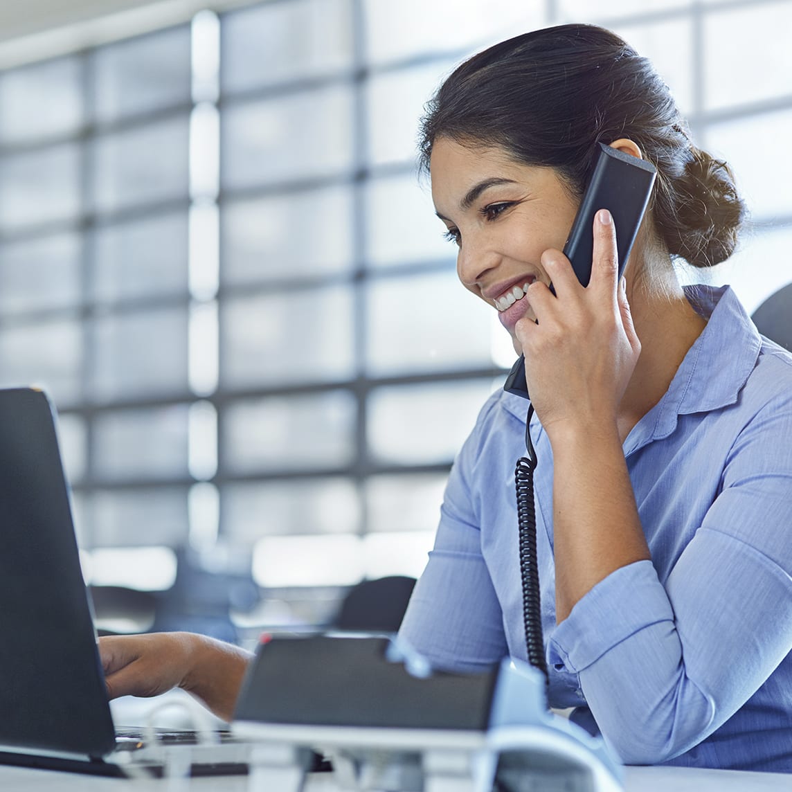 Woman at desk talking on phone while working on computer