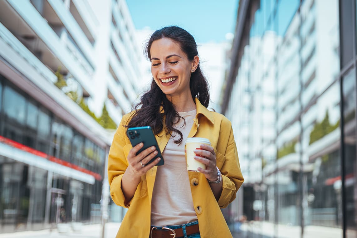 Happy woman walks outside with cell phone.