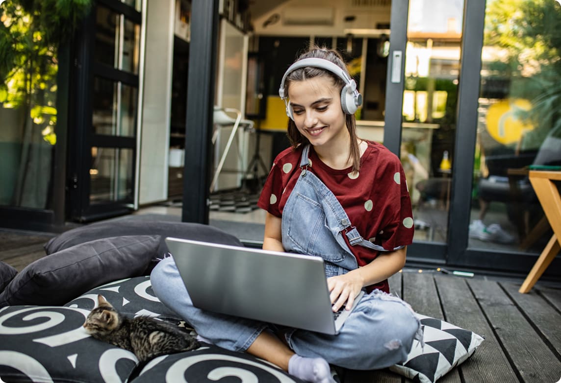 Young woman sits outside watching a movie on a laptop next to a cat.