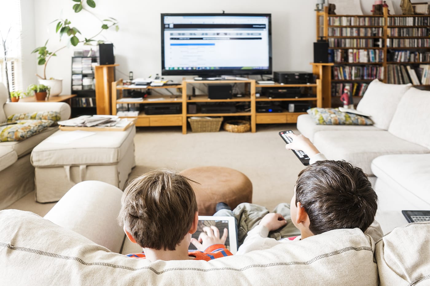 Two kids on couch watching tv and using tablet