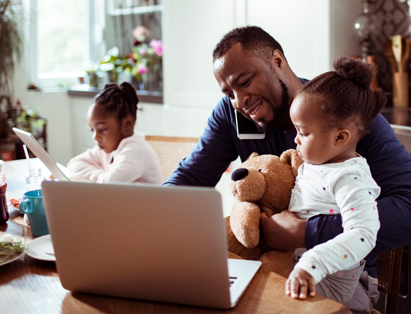 Father and his daughters, the father is talking on phone and using laptop