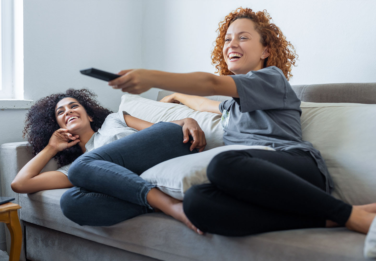 Two teen girls laying on a sofa watching TV
