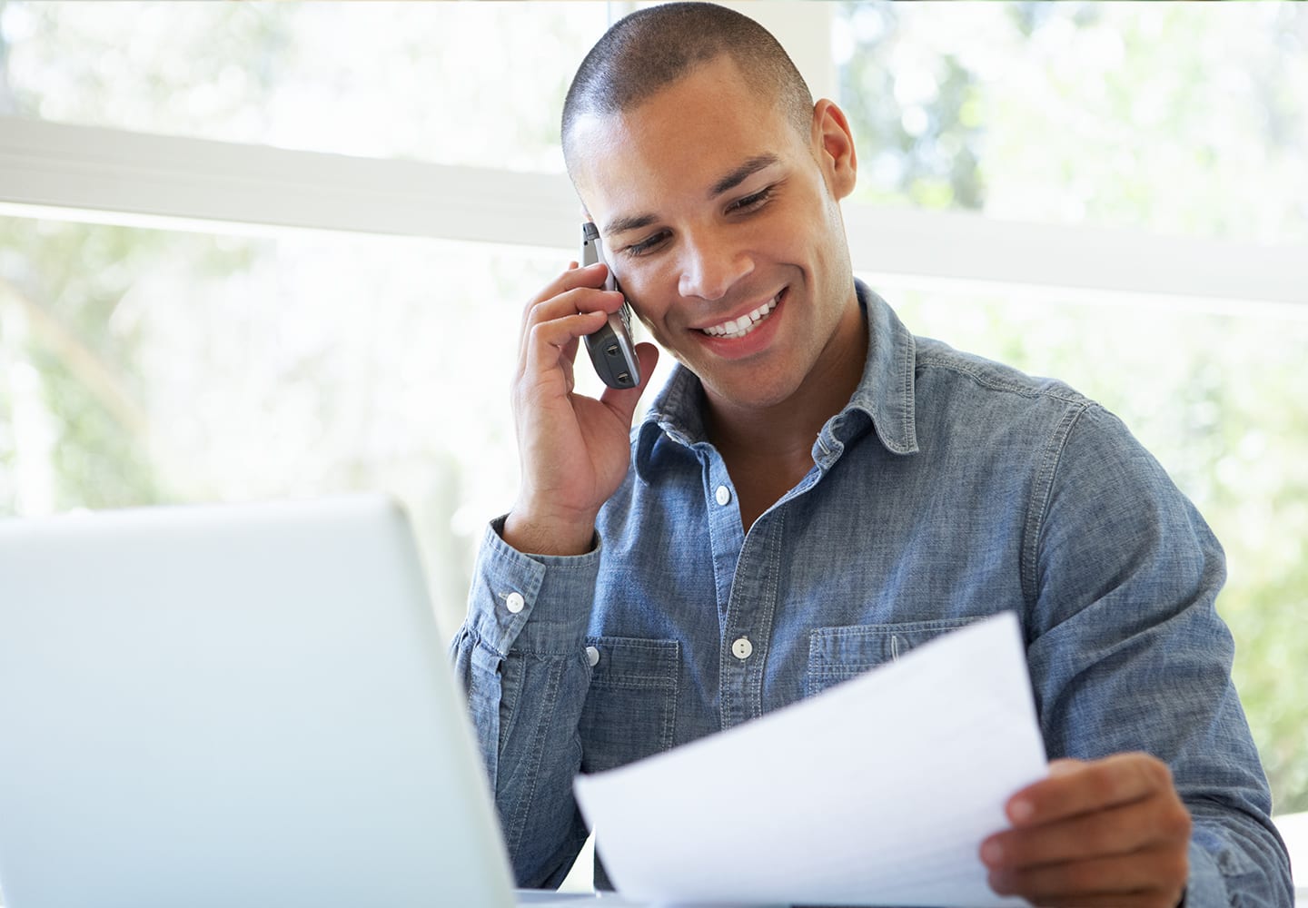 Man sitting next to laptop, talking on home phone and looking at papers