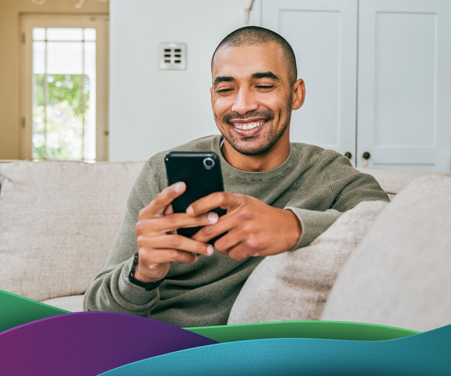 Happy man sitting on couch while looking at his phone.