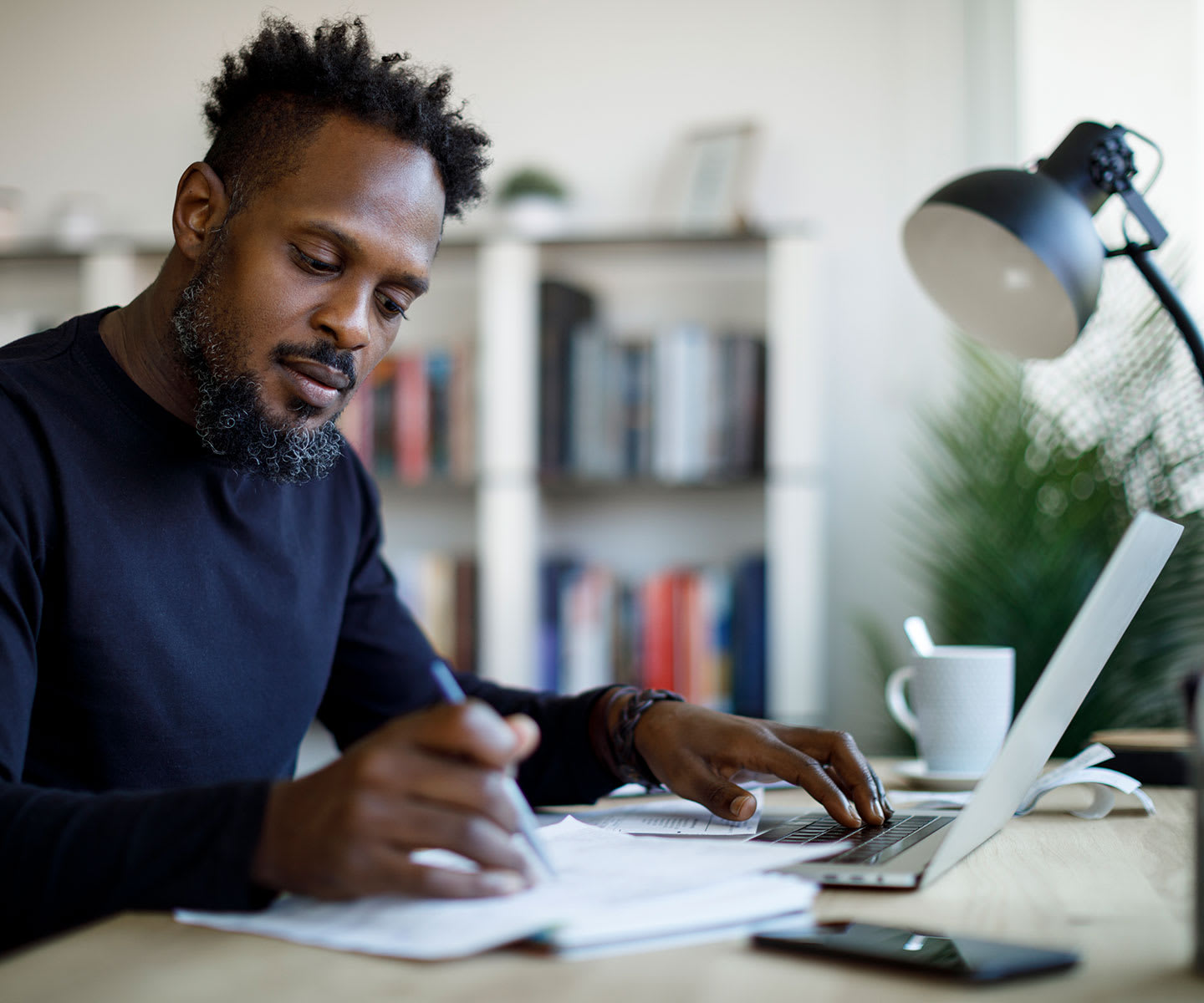 Man sitting at a desk, looking at papers next to his laptop