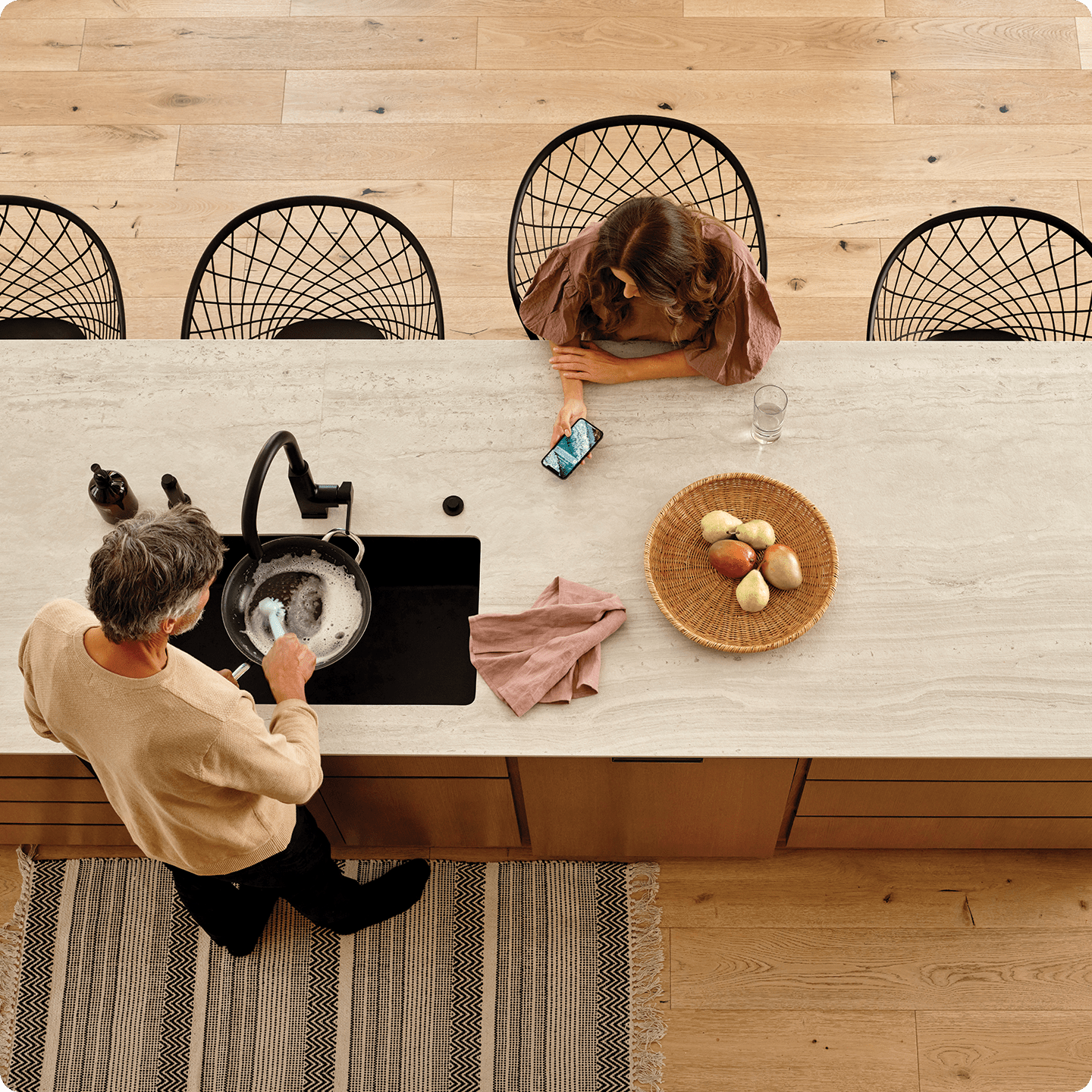 Woman receiving a Vivint monitoring notification in her kitchen while her husband does the dishes