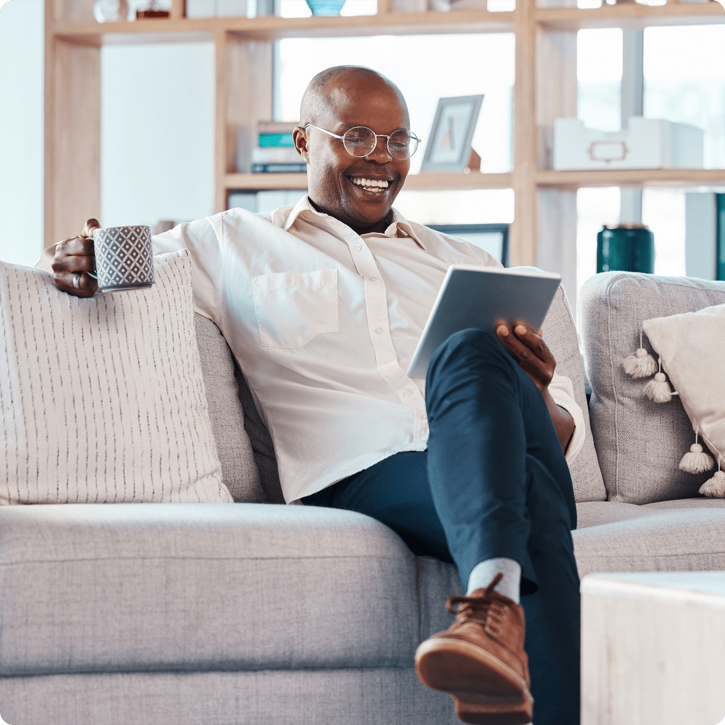 Man comfortable on the couch sipping coffee and looking at his tablet