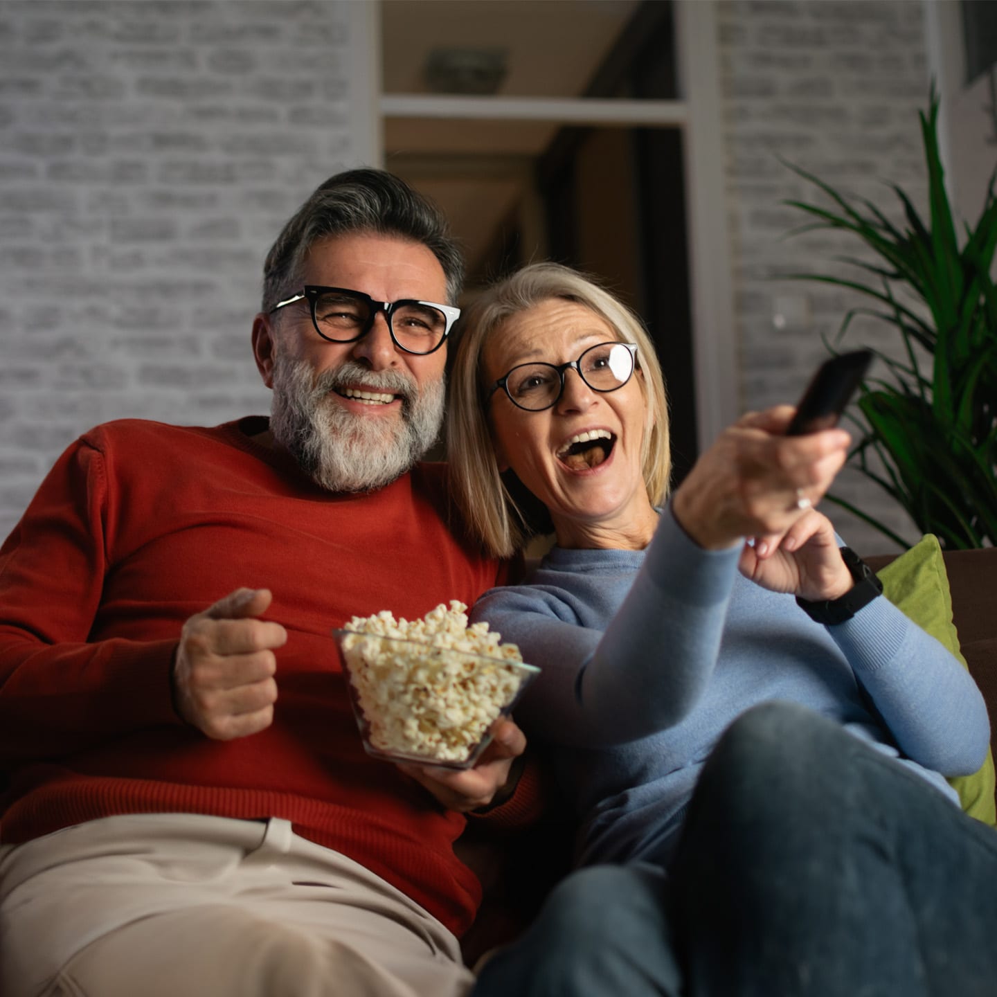 Senior couple laughing, eating popcorn, and watching their favorite TV show.