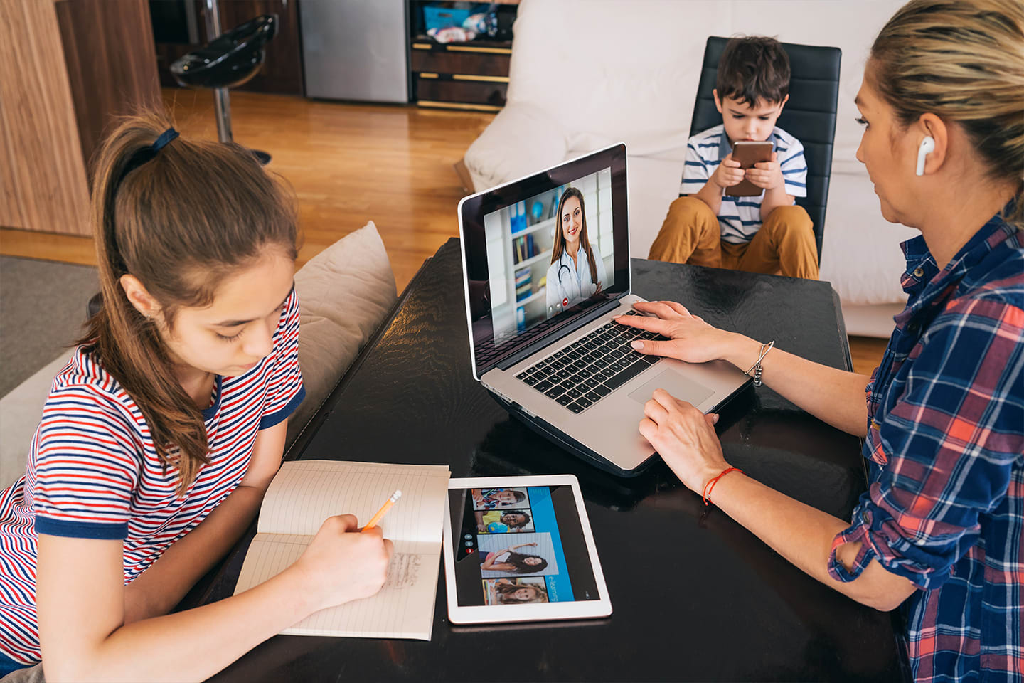 mother and two children sitting at table, using devices