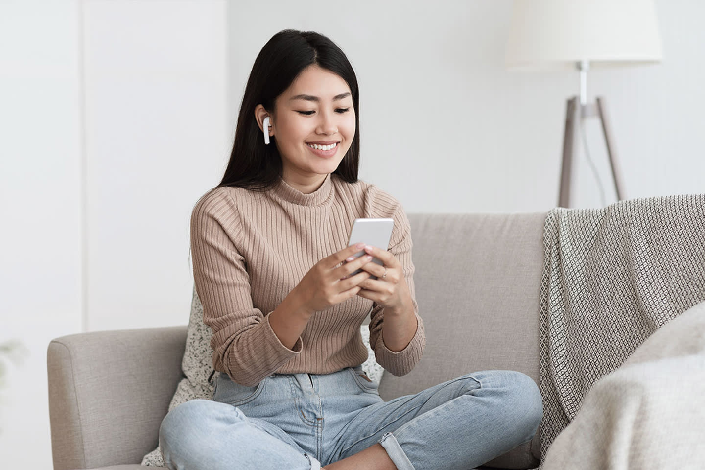 Black haired woman using her smartphone and wireless headphones.