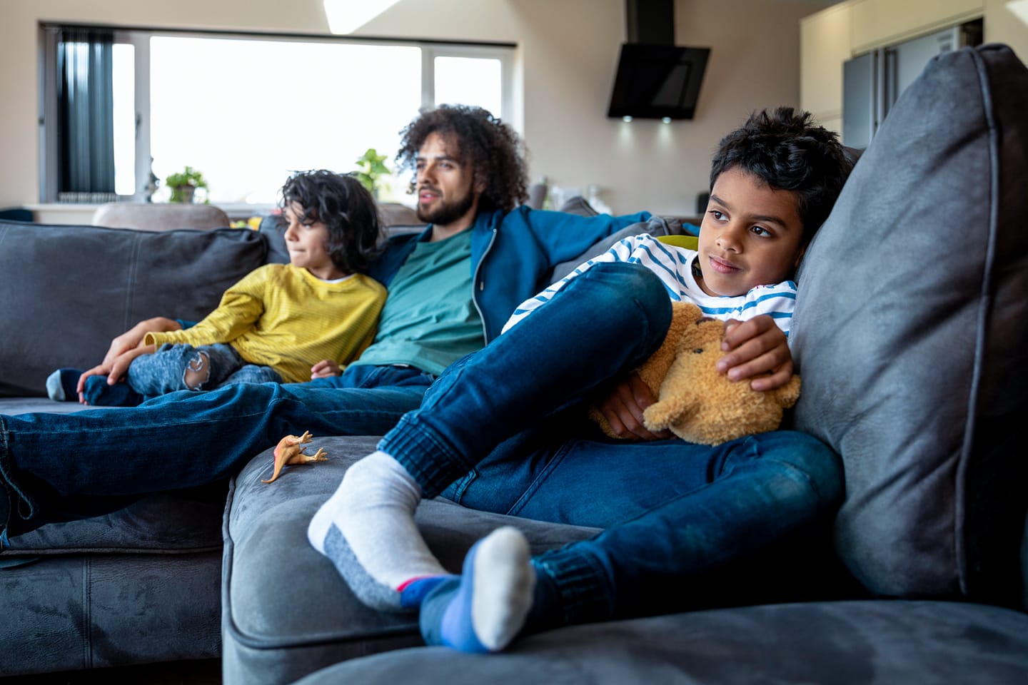 Un padre y dos hijos ven televisión juntos.