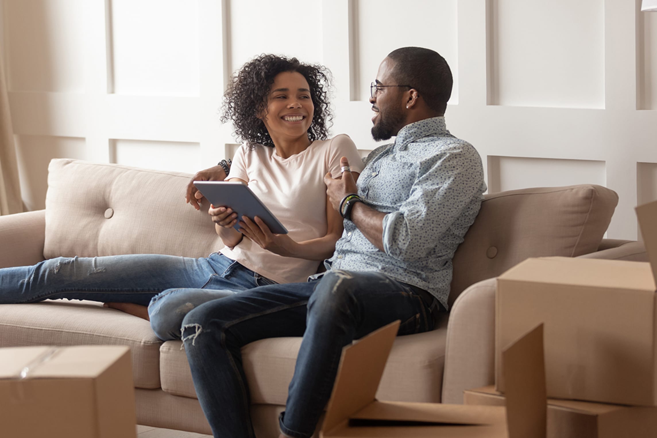 Happy couple uses a tablet together on a couch.