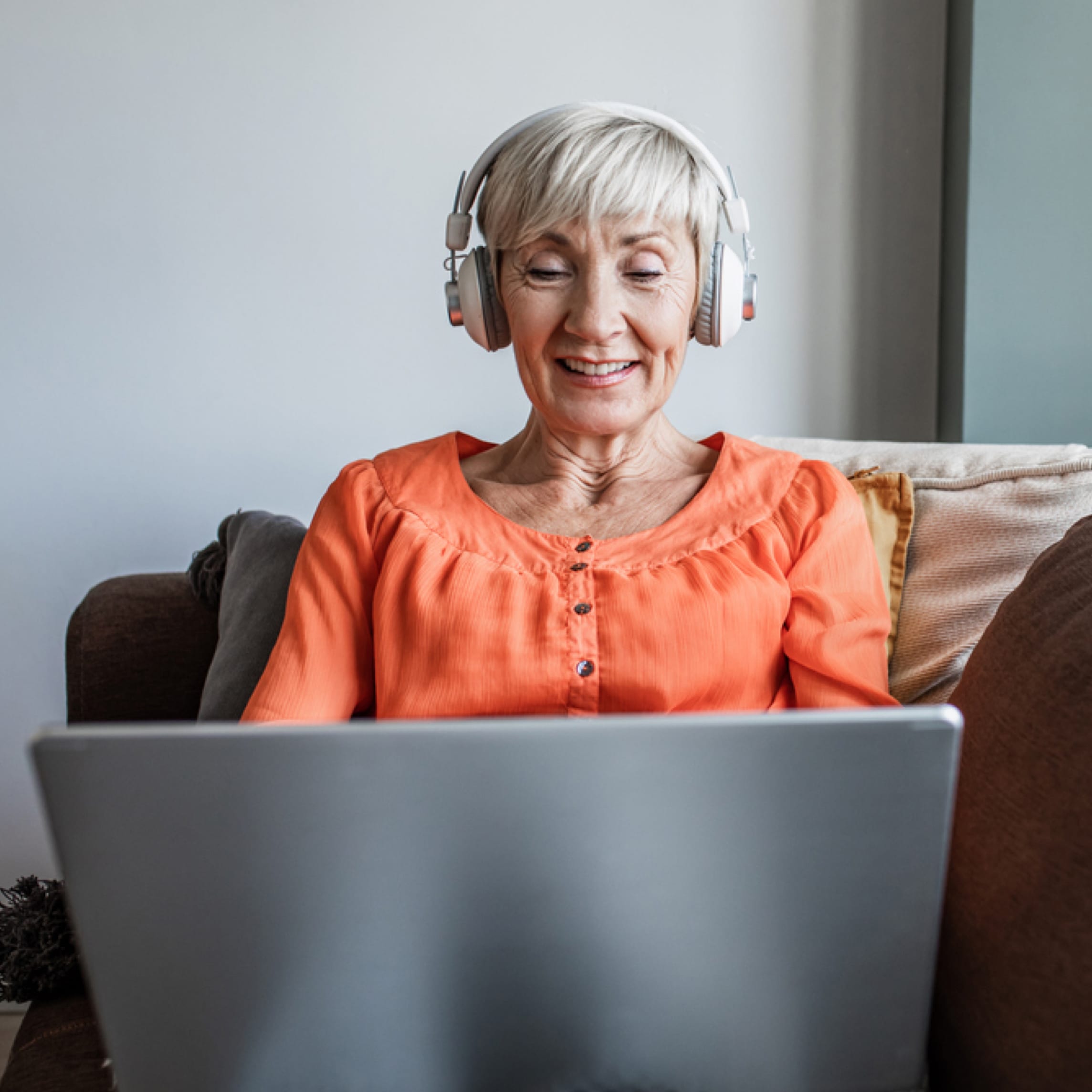 Woman sits on couch with laptop and headphones.