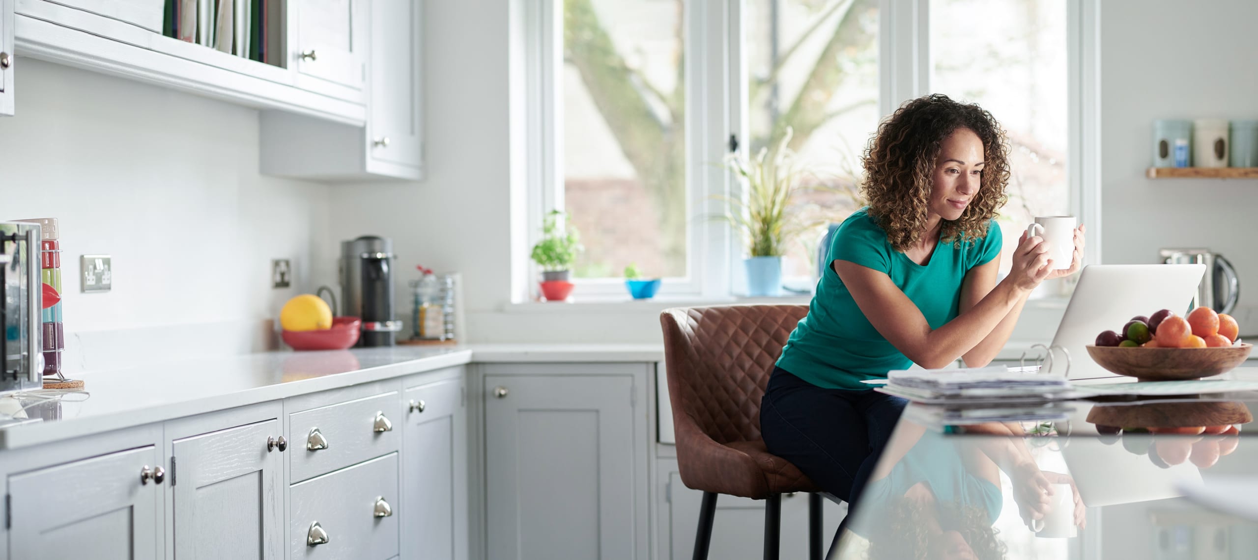 woman at kitchen counter drinking coffee using CenturyLink internet to check her email