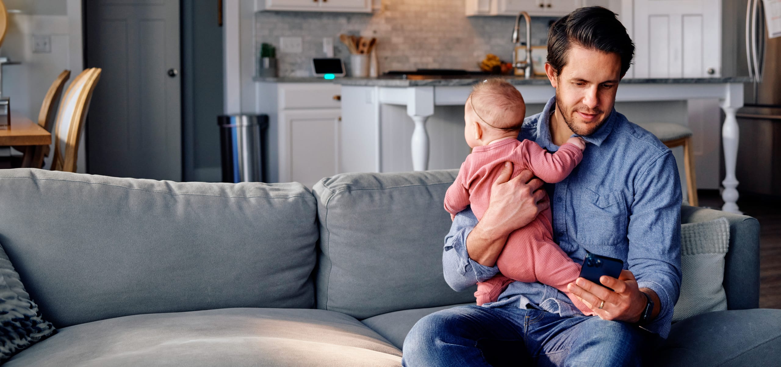 Dad holding baby and checking his smart devices paired with vivint