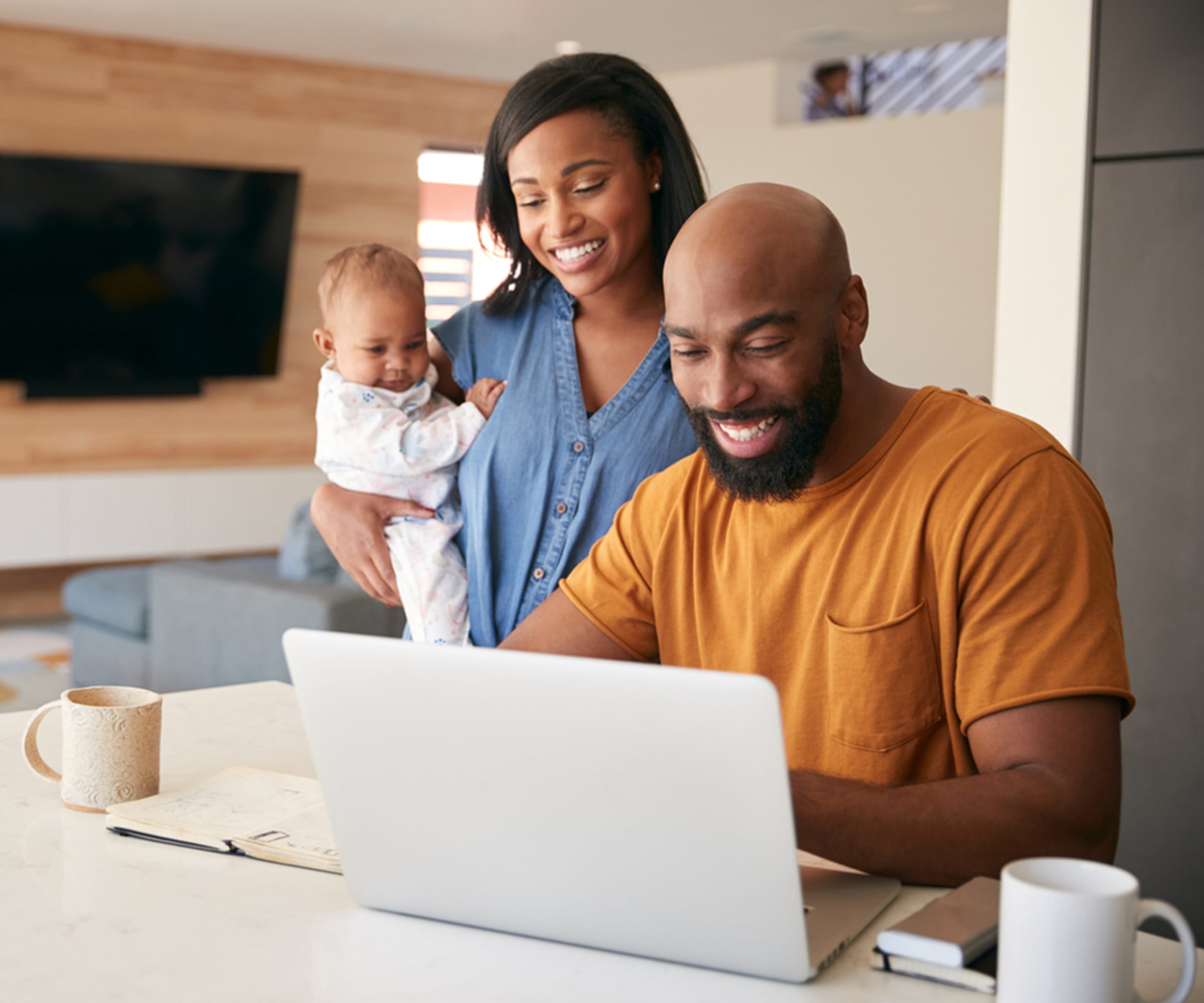 Couple with baby smile together while looking at a laptop