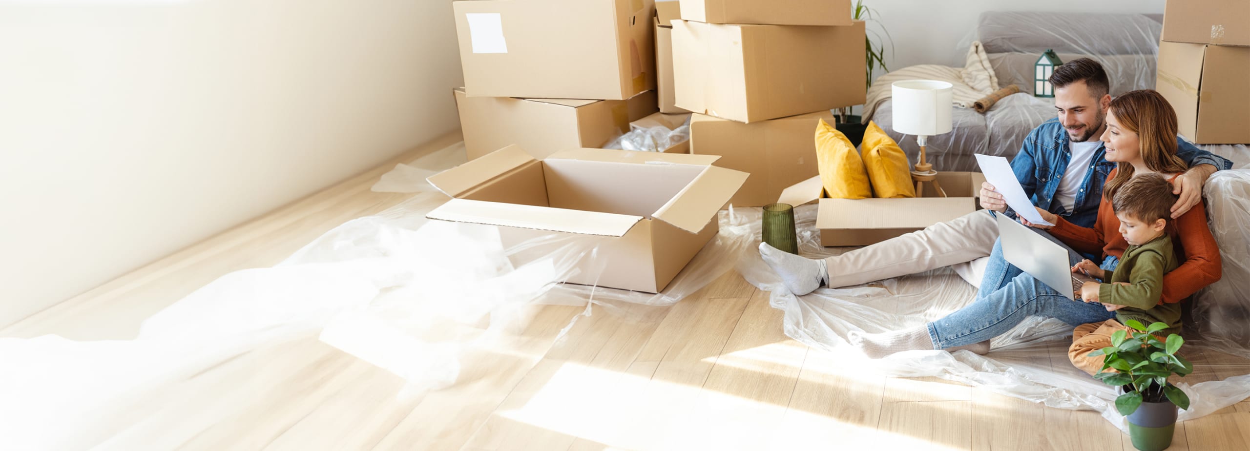 Happy family sits on floor of new home surrounded by boxes.