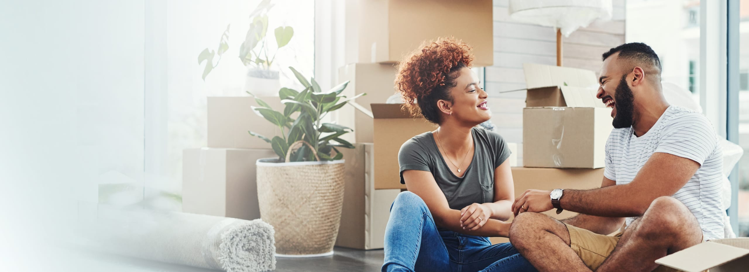 Couple laughing and talking, they are surrounded by moving boxes.