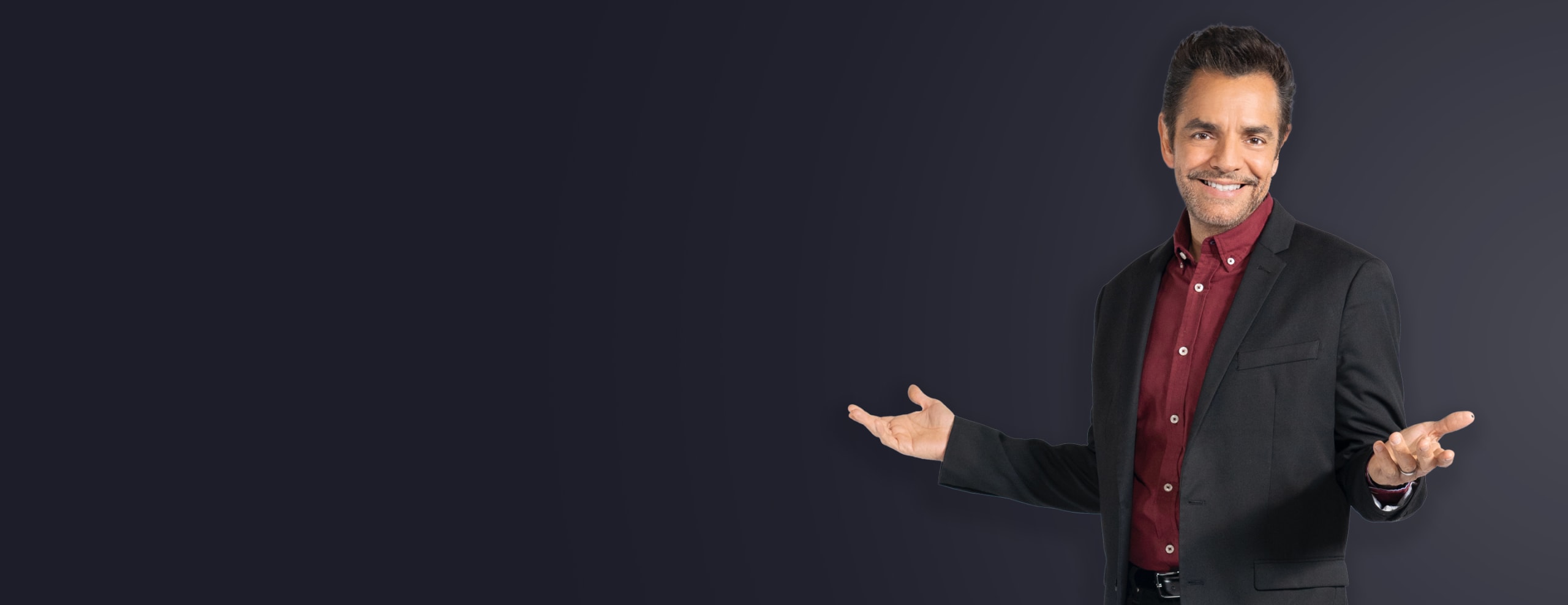 Eugenio Derbez con los brazos abiertos invitando. Lleva una camisa roja y una chaqueta deportiva negra.

Eugenio Derbez with open inviting arms. He's wearing a red shirt and black sport coat.