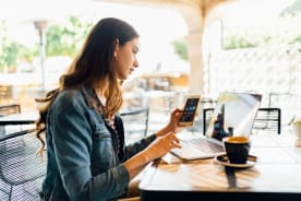 A woman works at desk with a laptop and smartphone