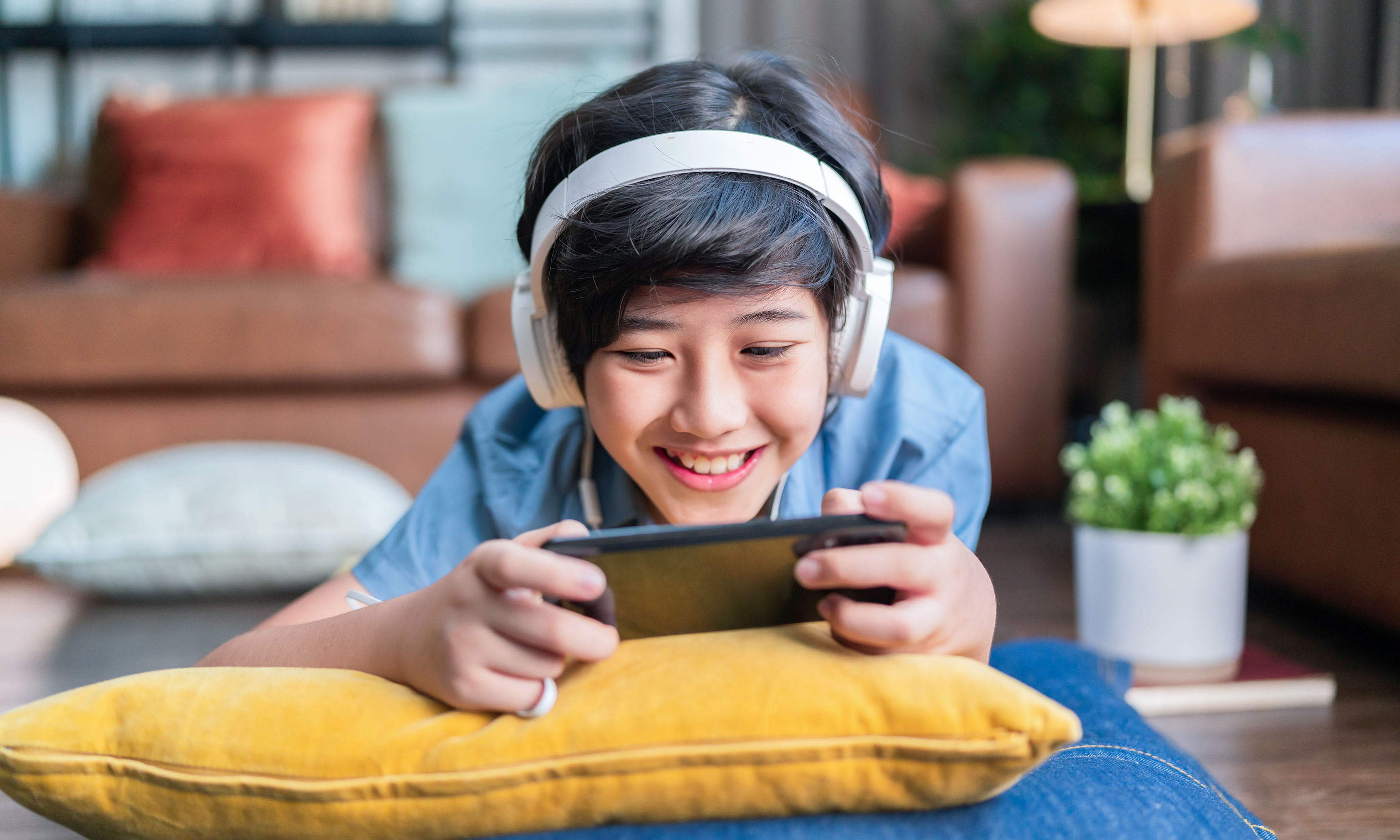 A teenage boy wearing headphones and streaming movies on his phone.